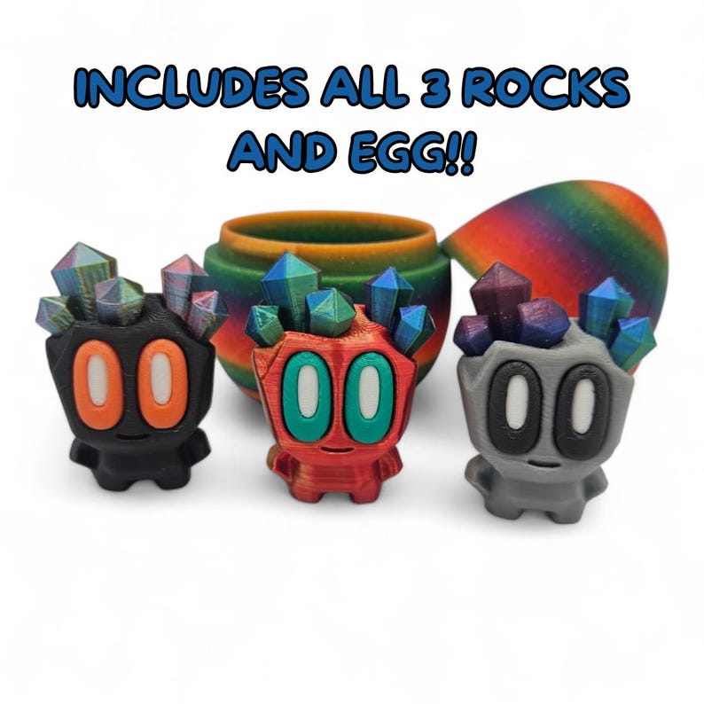 May include: Three colourful, stylised figures with crystal-like tops and the number "00" on their faces. The figures are black, red, and grey, with orange, teal, and blue accents. A rainbow-coloured egg and a matching pot are in the background. Text reads "INCLUDES ALL 3 ROCKS AND EGG!!"