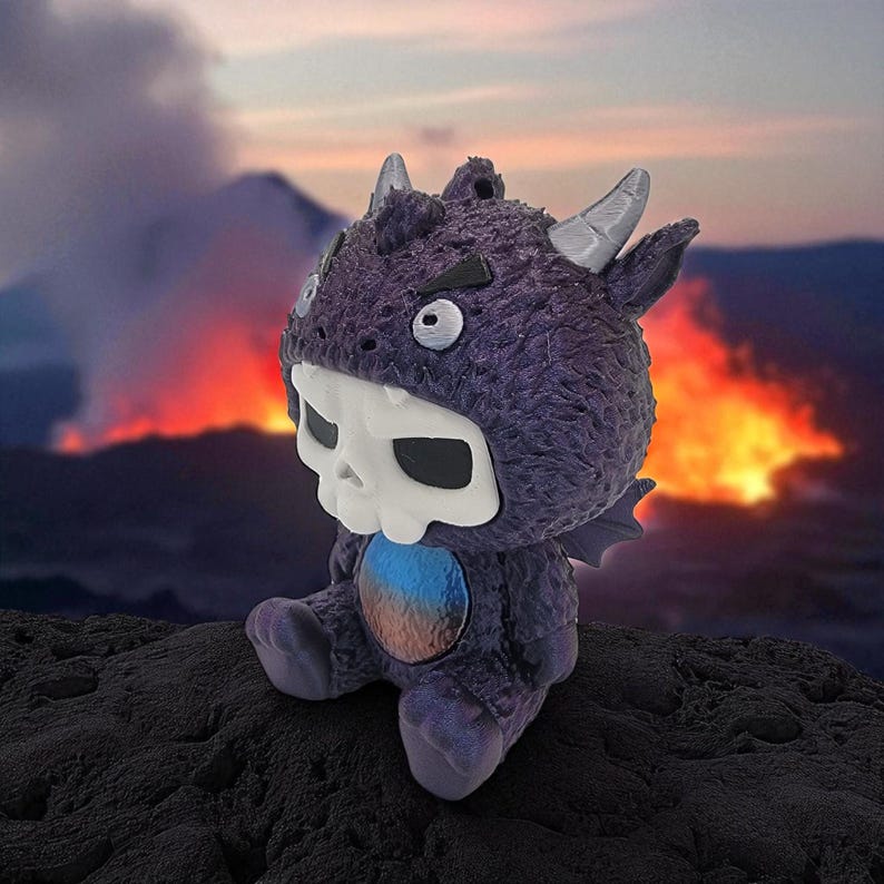 Puede incluir: Una criatura de peluche morada con una cara en forma de calavera y cuernos. La criatura tiene una panza azul y naranja y est&aacute; sentada sobre una superficie oscura y texturizada. El fondo presenta un paisaje volc&aacute;nico en llamas.