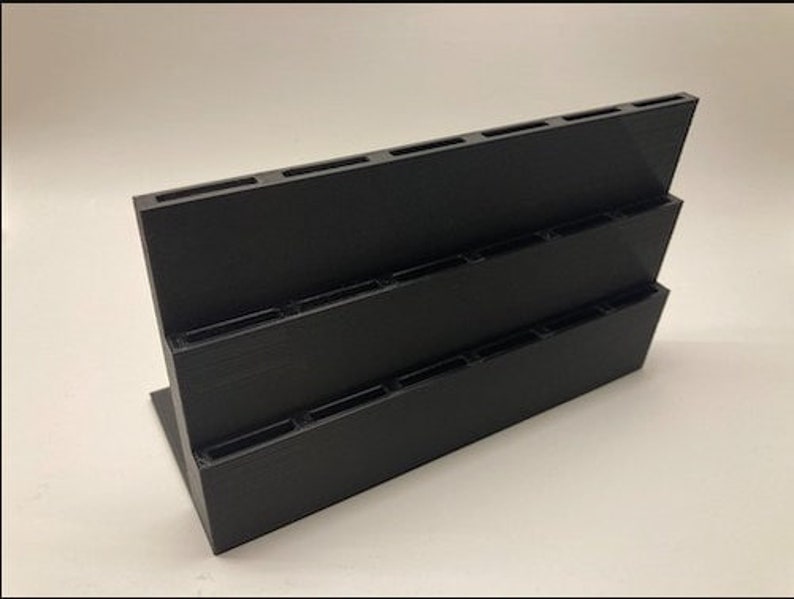 May include: Black plastic organizer with three tiers and multiple slots. The organizer is designed to hold small items, such as pens, pencils, or paintbrushes.