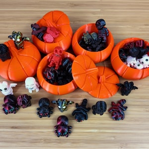 May include: A collection of small pumpkin-shaped containers filled with various Halloween-themed toys. The containers are orange and have a stem on top. The toys include spiders, skeletons, and ghosts.