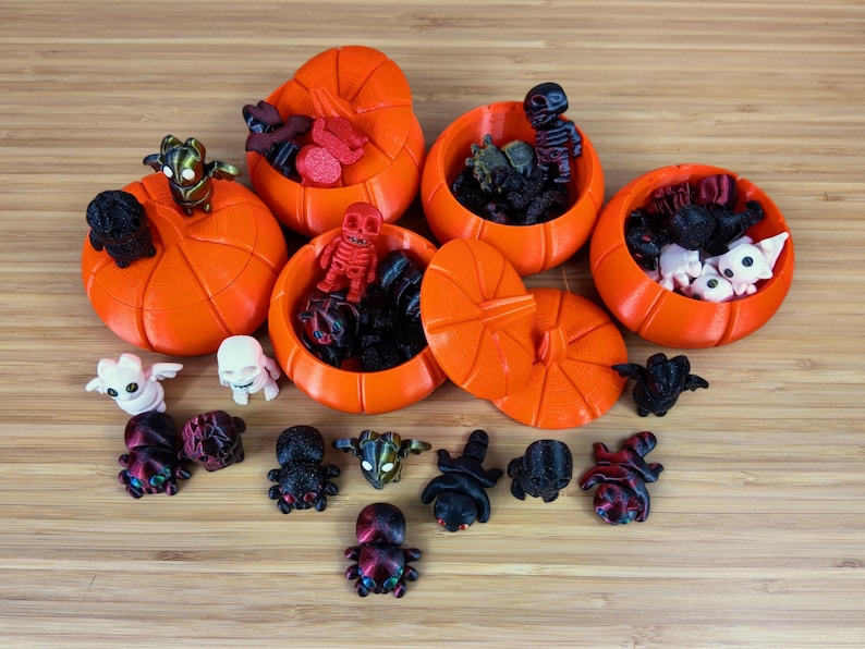 May include: A collection of small pumpkin-shaped containers filled with various Halloween-themed toys. The containers are orange and have a stem on top. The toys include spiders, skeletons, and ghosts.