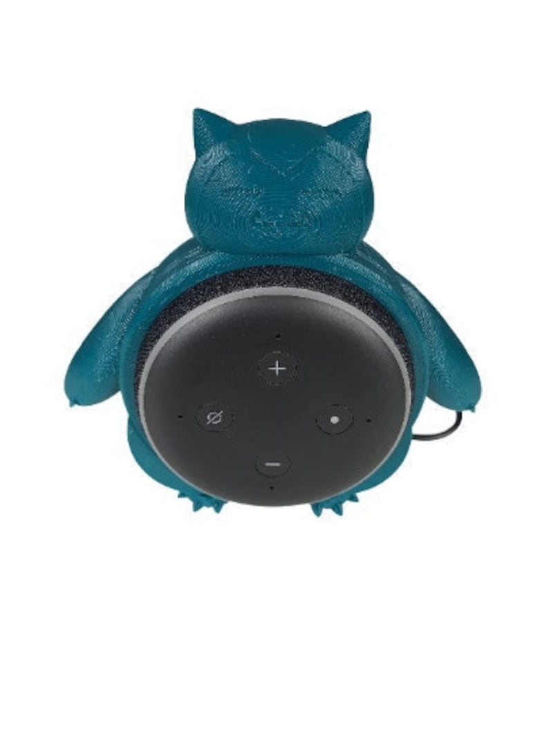May include: A teal blue 3D printed cat-shaped wall mount for an Amazon Echo Dot smart speaker. The speaker is visible in the mount, showing the black speaker controls.