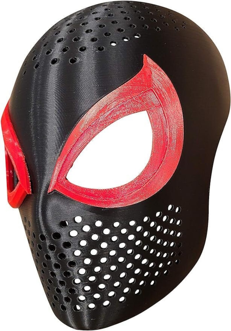 May include: Black and red superhero mask with a textured finish. The mask features large eye openings outlined in red and a series of small ventilation holes. The design is reminiscent of a comic book character.
