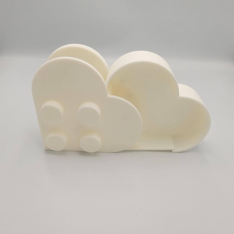 May include: A cream-colored, cloud-shaped napkin holder. The holder has a rounded design with four circular details on the front. The holder is made of a solid material and has a smooth surface. The design is modern and minimalist.