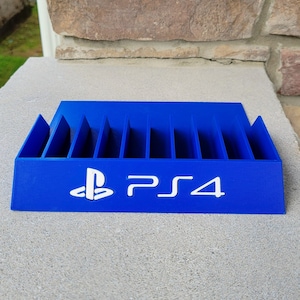 May include: A blue plastic video game case with slots for storing game discs. The case has the PlayStation logo and the text "PS4" printed on the front.