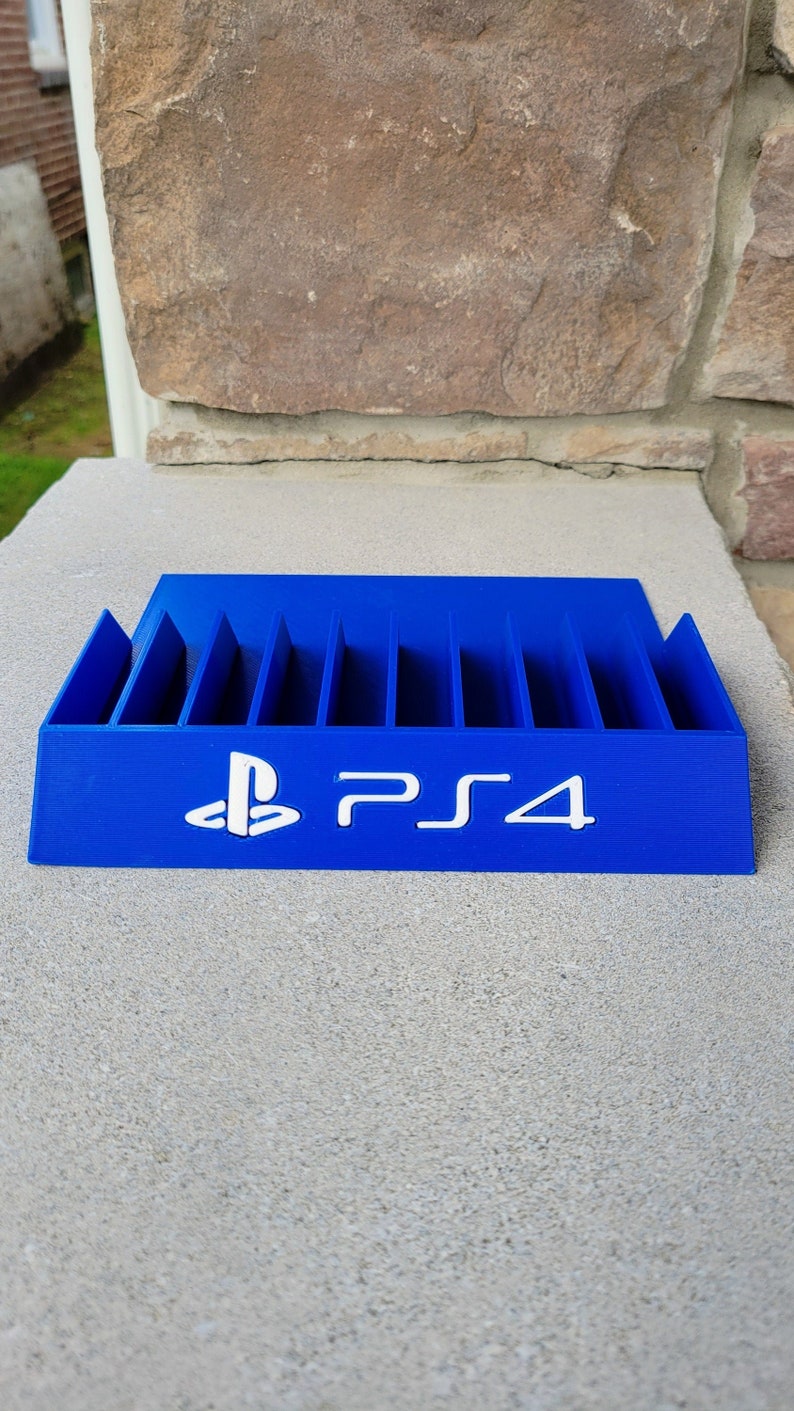 May include: A blue plastic video game case with slots for storing game discs. The case has the PlayStation logo and the text "PS4" printed on the front.