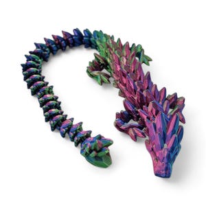 May include: A 3D printed iridescent lizard with a spiky, scaly texture. The lizard is green, blue, and purple with a metallic sheen. The lizard is posed in a curled position with its tail wrapped around its body.