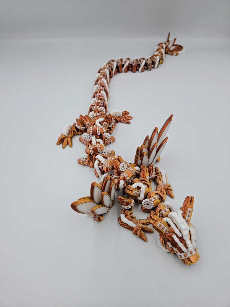 May include: A 3D printed, articulated dragon sculpture with a copper and white colour scheme. The dragon is posed in a crawling position with its head raised.