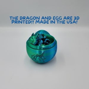 May include: A 3D printed, teal and green egg with a dragon inside. The egg is open and the dragon is visible. The egg has a unicorn design on the outside. The text "THE DRAGON AND EGG ARE 3D PRINTED!! MADE IN THE USA!" is visible above the egg.