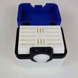 May include: A white and blue plastic storage box with a hinged lid and a small, round knob on the front. The box has a white interior with multiple slots for holding small items.