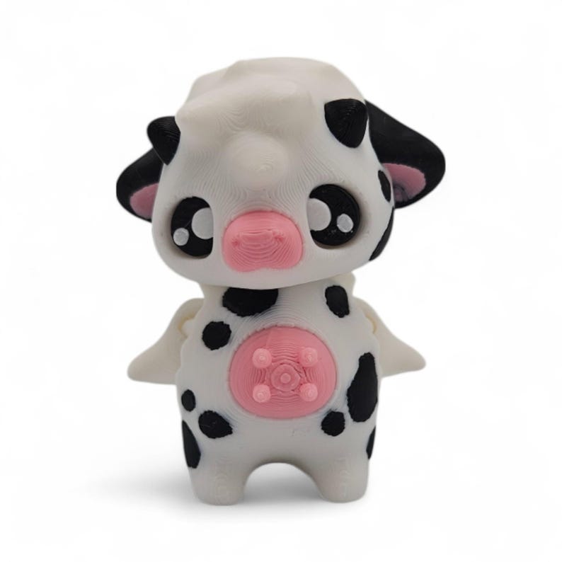 May include: A white and black spotted cow figurine with a pink nose and udder. The figurine has large black eyes and small wings. The cow figurine is a cute and whimsical design.