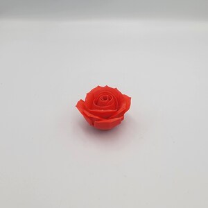 May include: A single, vibrant red rose. The rose is in full bloom, with tightly packed petals forming a spiral at the center. The petals have a slightly textured appearance. The rose is set against a plain white background.