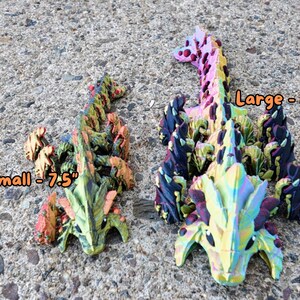 May include: Two colorful, 3D printed dragon figurines. The larger dragon is 11 inches long and the smaller dragon is 7.5 inches long. Both dragons have a green, yellow, orange, and black color scheme.