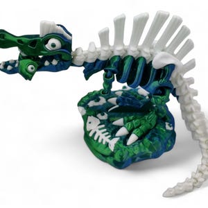 May include: A green and blue dinosaur skeleton toy with white bones. The dinosaur is sitting on a green and blue base with white fish bones.