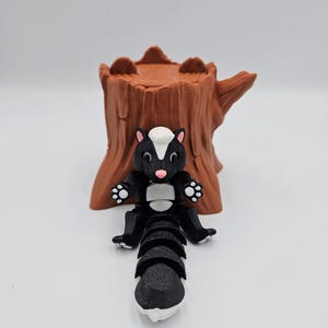 May include: A black and white skunk figurine with a segmented tail, sitting on a brown tree stump.