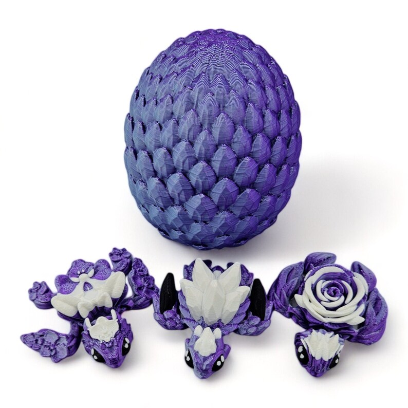 Puede incluir: Huevos de drag&oacute;n morados con tres dragones beb&eacute;s naciendo. Los huevos son texturizados y tienen un degradado de morado y blanco. Los dragones beb&eacute;s son morados y blancos con alas blancas y ojos negros.