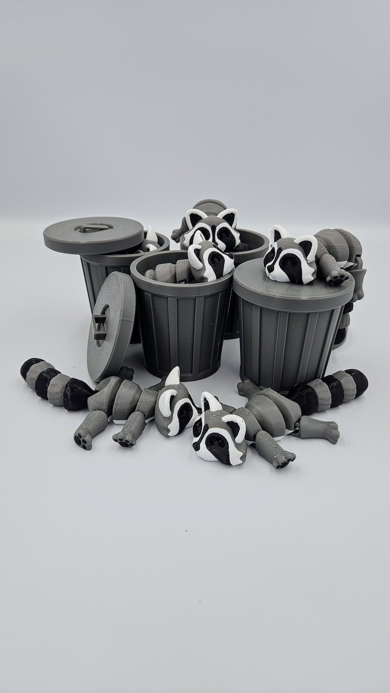 May include: Gray 3D-printed raccoon toys with black and white markings are scattered around several gray trash cans. Some raccoons are inside the cans, while others are lying nearby. The trash cans have lids.