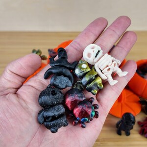 May include: A collection of small Halloween-themed figurines, including a skeleton, a spider, and a black cat. The figurines are made of plastic and are painted in various colors, including black, white, red, and green.