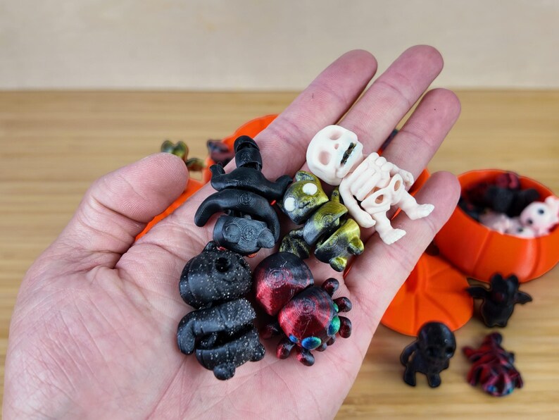 May include: A collection of small Halloween-themed figurines, including a skeleton, a spider, and a black cat. The figurines are made of plastic and are painted in various colors, including black, white, red, and green.