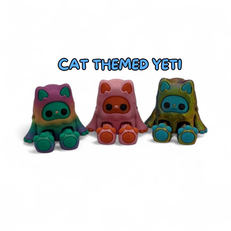 Puede incluir: Tres figuras de Yeti con tem&aacute;tica de gatos. Cada figura tiene una capucha con forma de gato y es de un color diferente: morado y verde, rosa y naranja, y verde y azul. El texto "CAT THEMED YETI" est&aacute; encima de las figuras.
