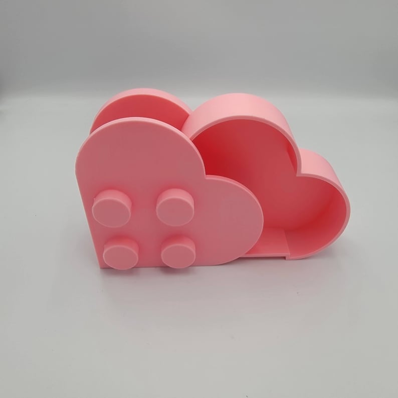May include: A pink desk organizer shaped like a cloud. The organizer has a heart-shaped front with four circular studs and a larger cloud-shaped compartment. The design is a playful, modern take on storage.
