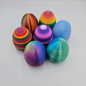 K&ouml;nnte beinhalten: Sechs bunte Ostereier, jedes mit einem anderen Muster und einer anderen Farbe. Die Eier sind aus Kunststoff und haben eine glatte, gl&auml;nzende Oberfl&auml;che. Die Farben umfassen Regenbogen, Lila, Blau, Gr&uuml;n und Kupfer.