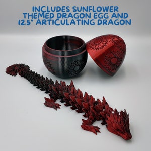Puede incluir: Un juguete de drag&oacute;n articulado rojo con detalles de girasol, de 31,75 cm de largo. El drag&oacute;n est&aacute; posado sobre una superficie blanca junto a un huevo de drag&oacute;n con tem&aacute;tica de girasol cerrado. El huevo est&aacute; abierto y el interior es negro.