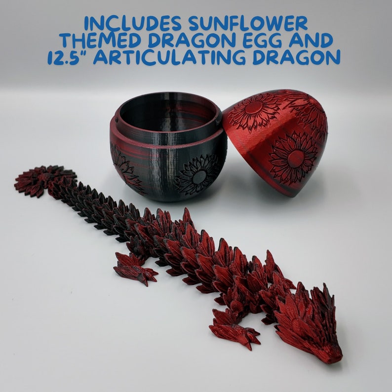 Puede incluir: Un juguete de drag&oacute;n articulado rojo con detalles de girasol, de 31,75 cm de largo. El drag&oacute;n est&aacute; posado sobre una superficie blanca junto a un huevo de drag&oacute;n con tem&aacute;tica de girasol cerrado. El huevo est&aacute; abierto y el interior es negro.