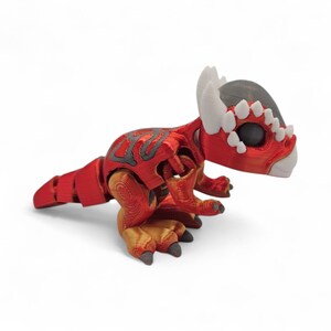 May include: A red and gray 3D-printed dinosaur figurine with a detailed design. The dinosaur has a segmented body, with a head featuring white horns and a gray top. The feet are a mix of gold and gray, and the overall design is intricate.