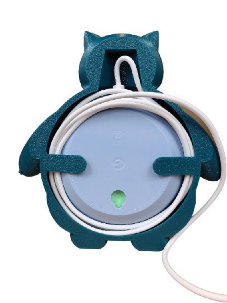 May include: A teal blue 3D printed wall mount for a smart speaker. The mount is shaped like a cartoon penguin and has a hole in the back for the speaker's power cord. The mount is designed to hold the speaker and its cord neatly.