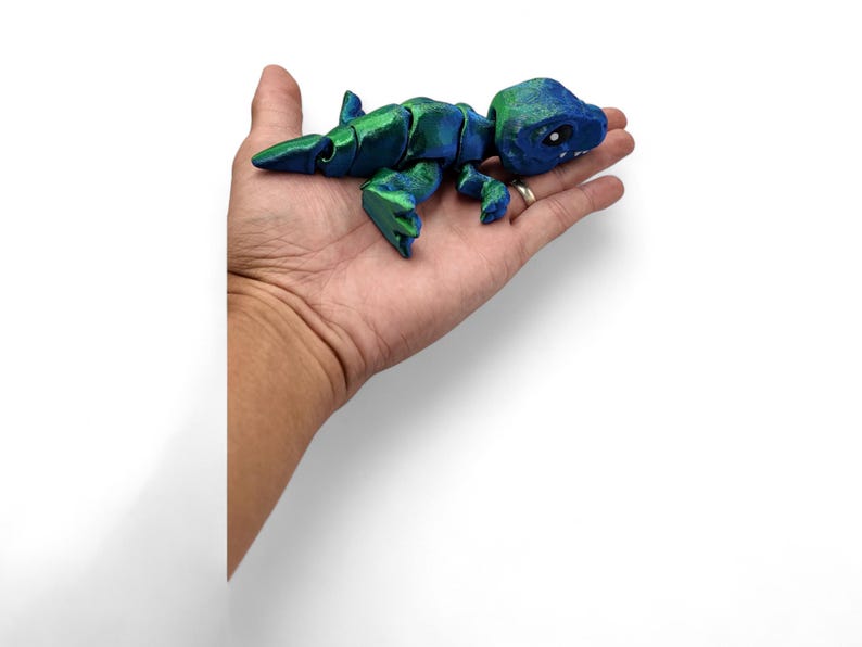 May include: A small, blue and green articulated dinosaur toy. The dinosaur is posed in a walking position with its head turned to the side. The toy is made of plastic and has a smooth, shiny finish.