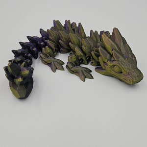 K&ouml;nnte beinhalten: Eine 3D-gedruckte Drachenfigur mit einem gr&uuml;n-violetten, irisierenden Finish. Der Drache ist in einer kriechenden Position mit erhobenem Kopf und eingerolltem Schwanz dargestellt.