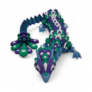 May include: A colorful articulated dragon figurine in shades of blue, green, purple, and white. The dragon has a detailed, segmented body and a peacock-like tail. The head is pointed, and the feet are small and clawed.