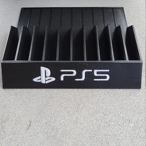 May include: Black plastic game case with slots for storing video game discs. The case has a white PlayStation logo and the text "PS5" printed on the front.