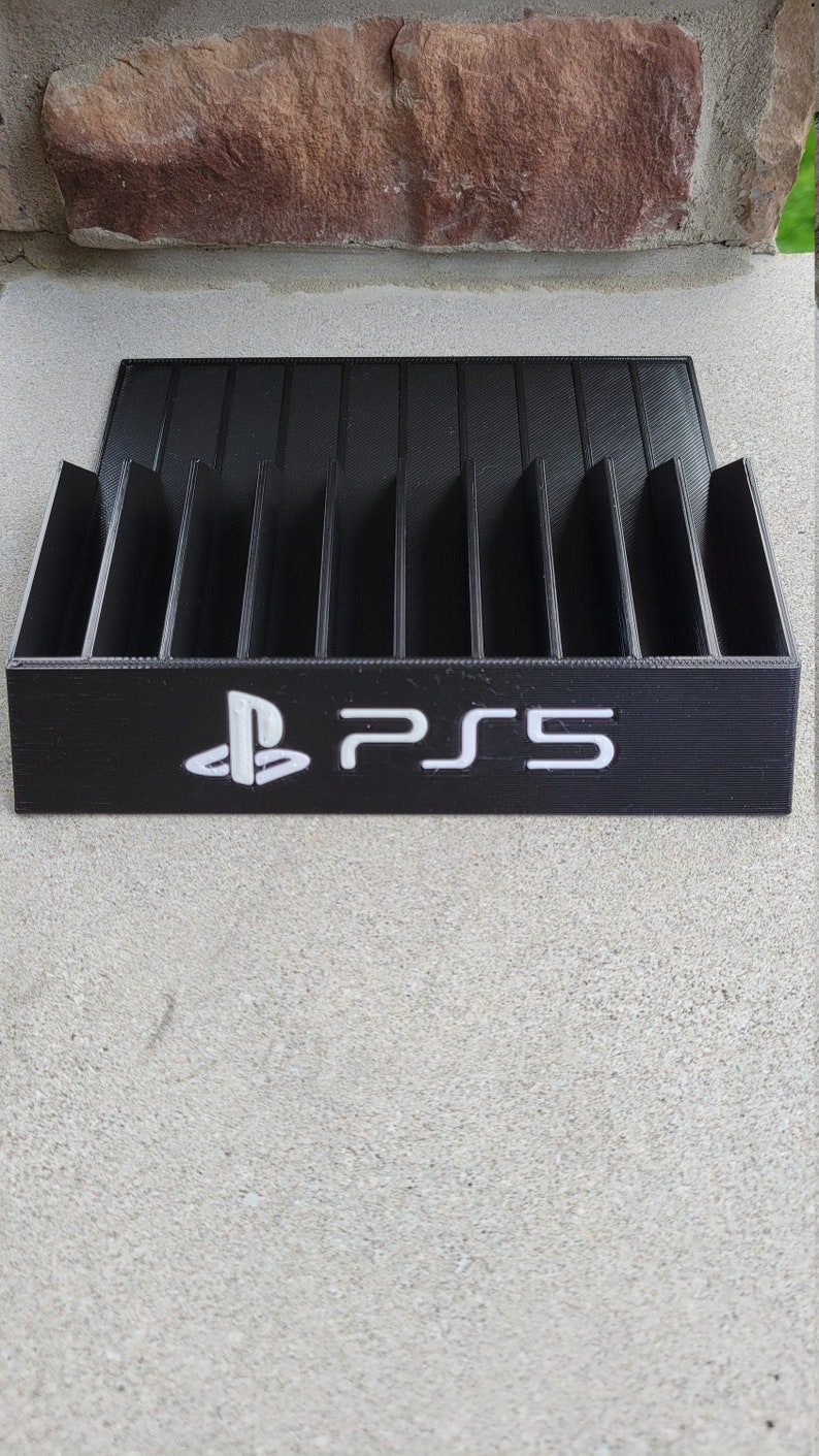 May include: Black plastic game case with slots for storing video game discs. The case has a white PlayStation logo and the text "PS5" printed on the front.