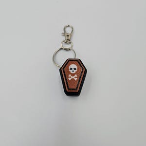May include: A black and brown coffin-shaped keychain with a white skull and crossbones design.