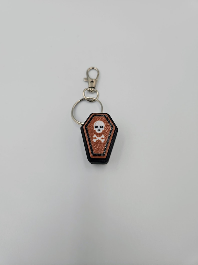 May include: A black and brown coffin-shaped keychain with a white skull and crossbones design.