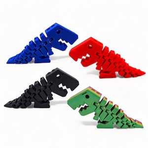 May include: Four 3D printed dinosaur toys in different colors: blue, red, black, and green. The dinosaurs are all in the same pose, with their mouths open and their tails curled up.