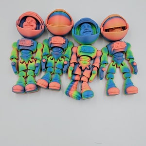 May include: Four colorful astronaut figurines with rainbow paint and articulated limbs. Each astronaut has a removable helmet with a face inside.