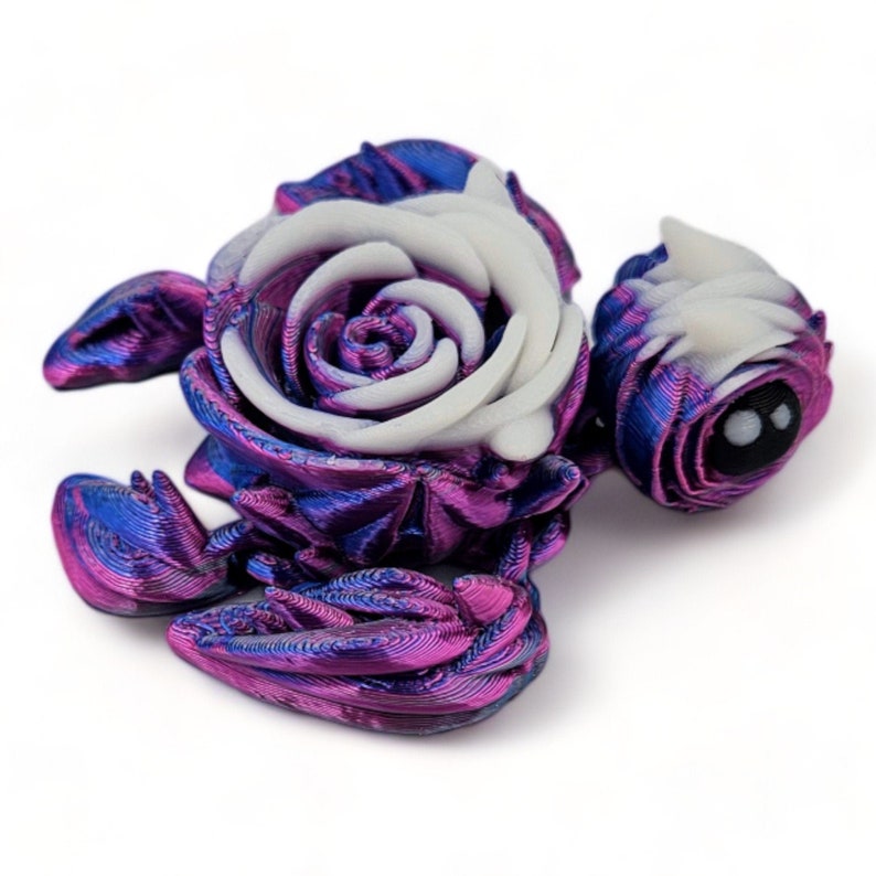 Puede incluir: Una escultura de un escorpi&oacute;n impresa en 3D con una rosa blanca en la espalda. El escorpi&oacute;n es de color morado oscuro y azul con un brillo met&aacute;lico.