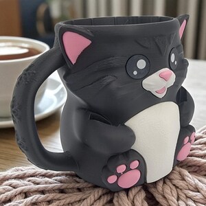 May include: A black cat-shaped mug with pink accents on the ears and paws. The mug has a white chest and a pink nose and mouth. The handle is shaped like a cat's tail. The mug is sitting on a pink knitted surface.