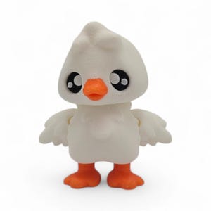 May include: A white 3D-printed duck figurine with an orange beak and feet. The duck has large, black eyes and small wings. The figurine is standing upright and has a smooth, textured surface.
