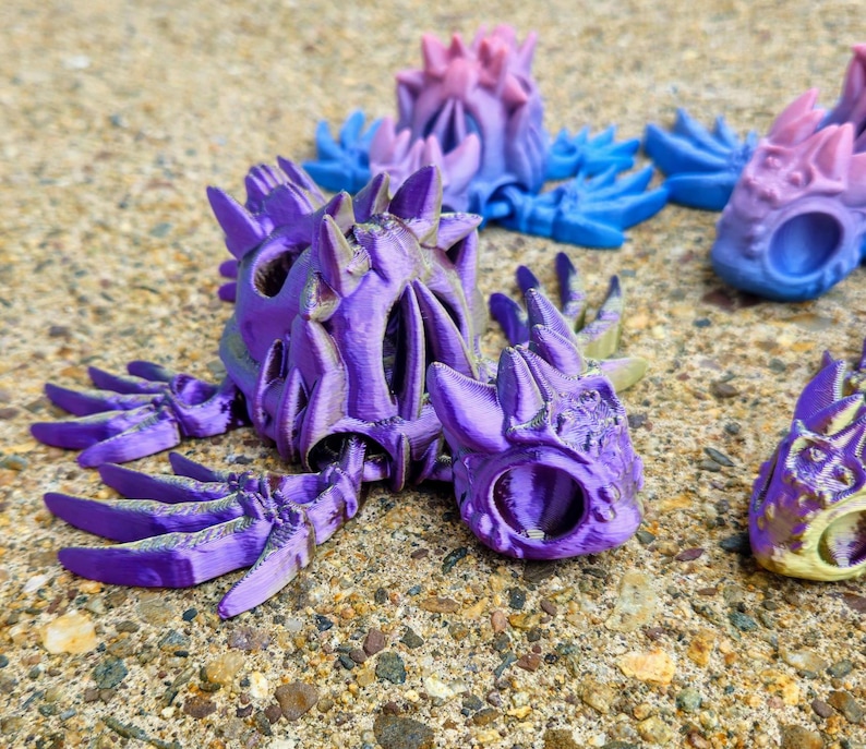 Peut inclure: Figurines de dragon imprim&eacute;es en 3D de couleur violette, bleue et rose avec des d&eacute;tails complexes et un design squelettique. Les dragons sont pos&eacute;s dans diff&eacute;rentes positions, les ailes d&eacute;ploy&eacute;es et les queues enroul&eacute;es.