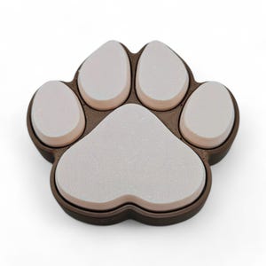 May include: A brown and white paw print-shaped object. The paw print has five white pads with a brown border. The object is likely a decorative item or a pet-themed accessory.