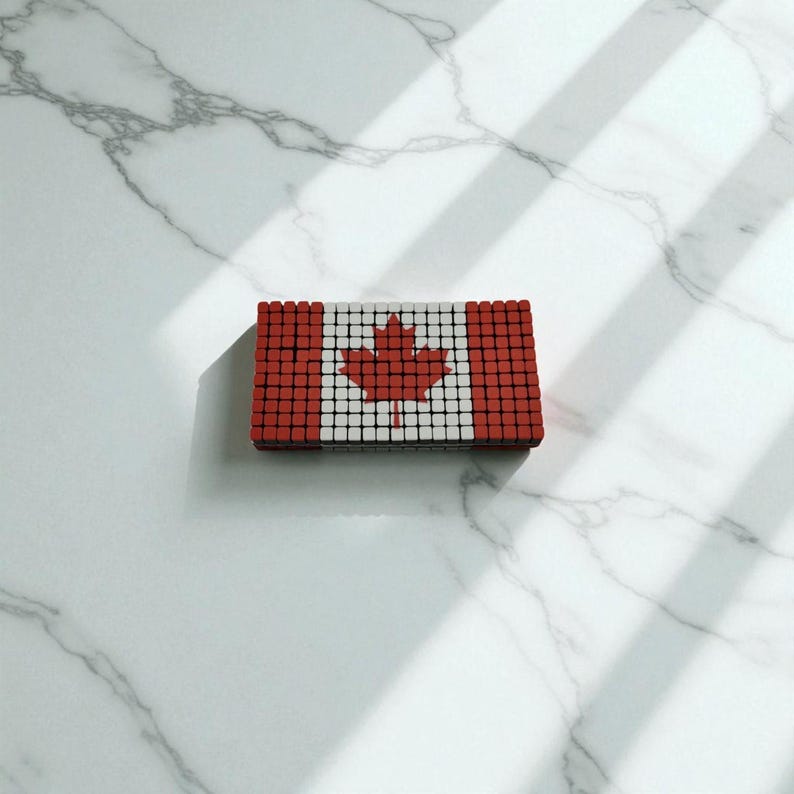 Pode incluir: Um objeto retangular que se assemelha &agrave; bandeira canadense, composto por pequenos quadrados vermelhos, brancos e pretos. A bandeira apresenta uma folha de bordo vermelha no centro. O objeto est&aacute; sobre uma superf&iacute;cie de m&aacute;rmore branco.