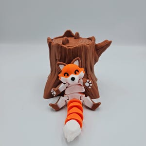 May include: A small, orange and white fox figurine with a segmented tail, sitting on a brown tree stump.