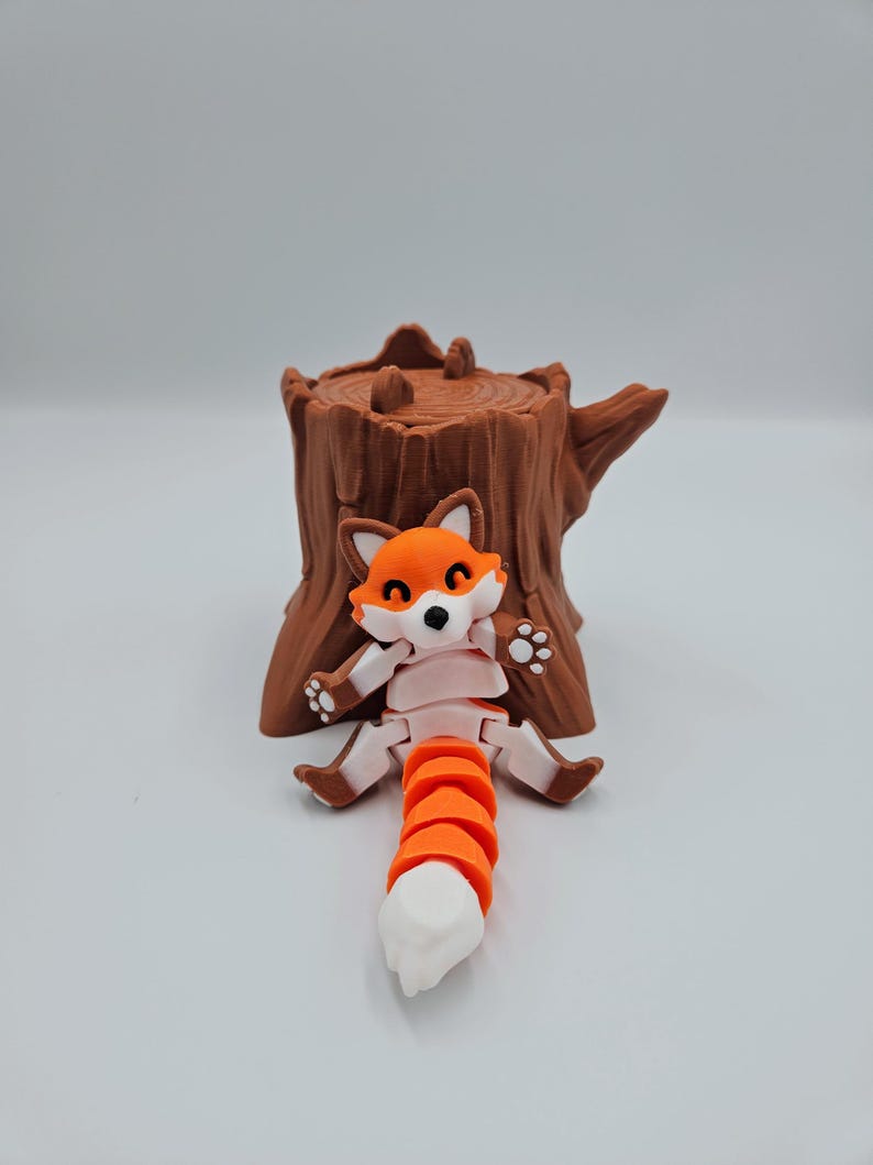 May include: A small, orange and white fox figurine with a segmented tail, sitting on a brown tree stump.