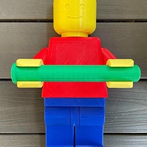 K&ouml;nnte beinhalten: Eine farbenfrohe, 3D-gedruckte Lego-Figur mit gelbem Kopf, rotem Torso, blauen Beinen und einer gr&uuml;nen Stange in den Armen. Die Figur ist so gestaltet, dass sie einer klassischen Lego-Minifigur &auml;hnelt, mit einem l&auml;chelnden Gesicht auf dem Kopf.