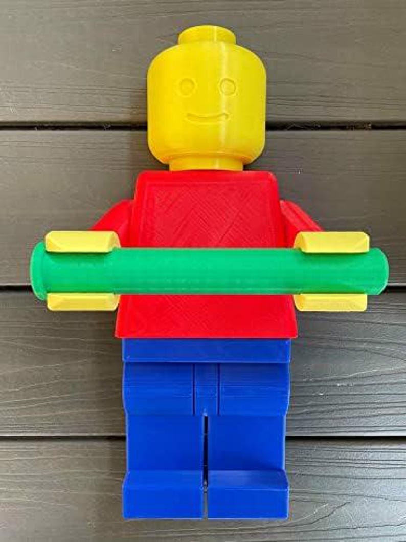 K&ouml;nnte beinhalten: Eine farbenfrohe, 3D-gedruckte Lego-Figur mit gelbem Kopf, rotem Torso, blauen Beinen und einer gr&uuml;nen Stange in den Armen. Die Figur ist so gestaltet, dass sie einer klassischen Lego-Minifigur &auml;hnelt, mit einem l&auml;chelnden Gesicht auf dem Kopf.