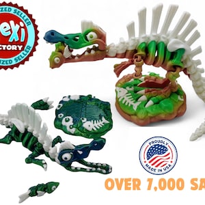 May include: A green and white articulated dinosaur skeleton toy with a base. The dinosaur has a large head with a toothy grin and large eyes. The base is green and brown with a fish bone design. The toy is made in the USA and has sold over 7,000 units.